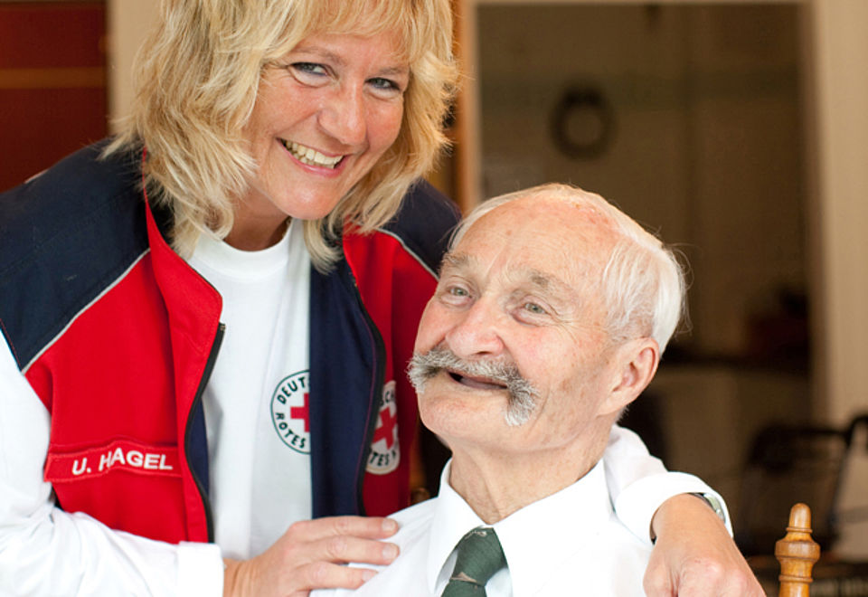 Ein lachender Senior mit einer DRK-Mitarbeiterin